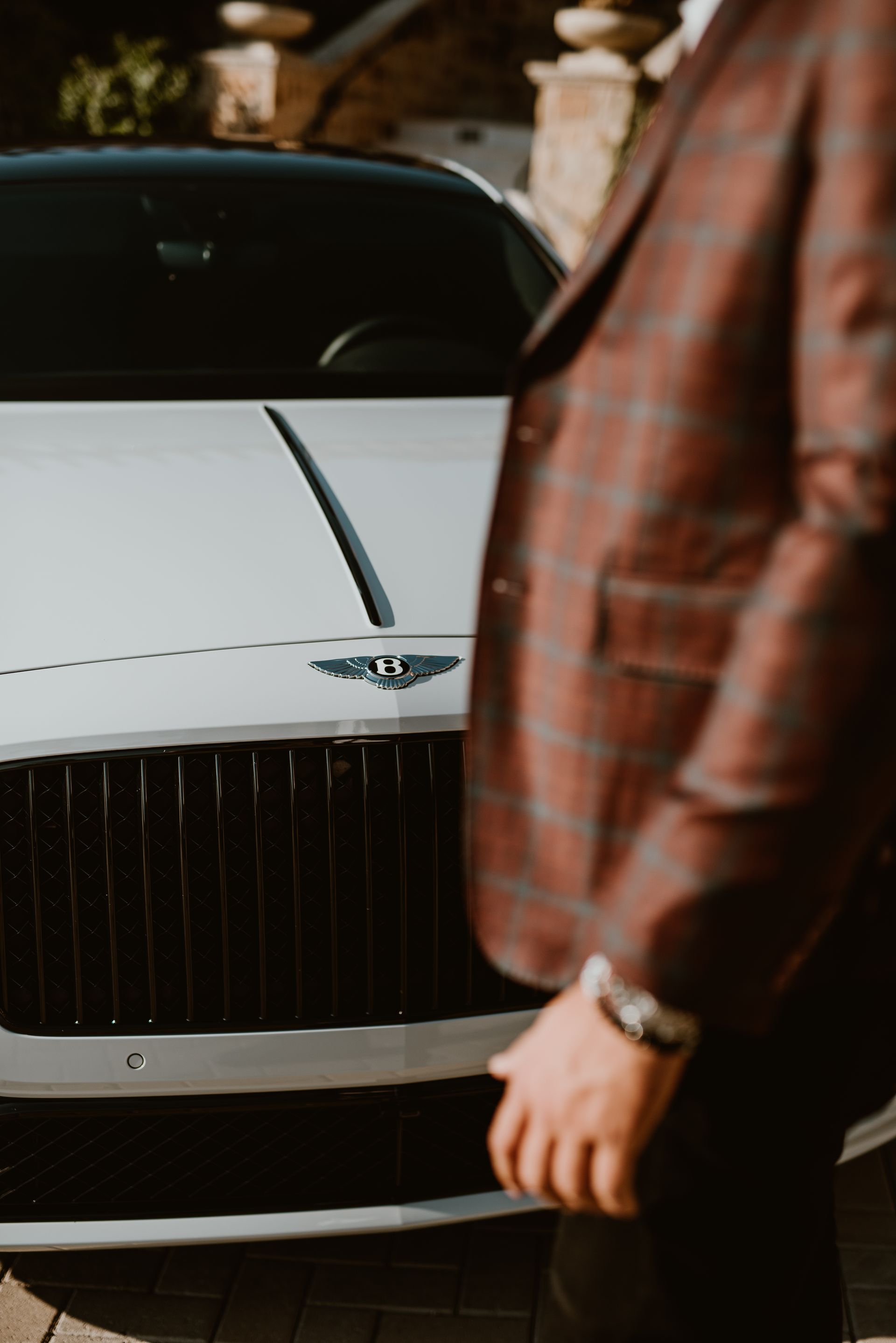 A man in a suit is standing in front of a bentley car.