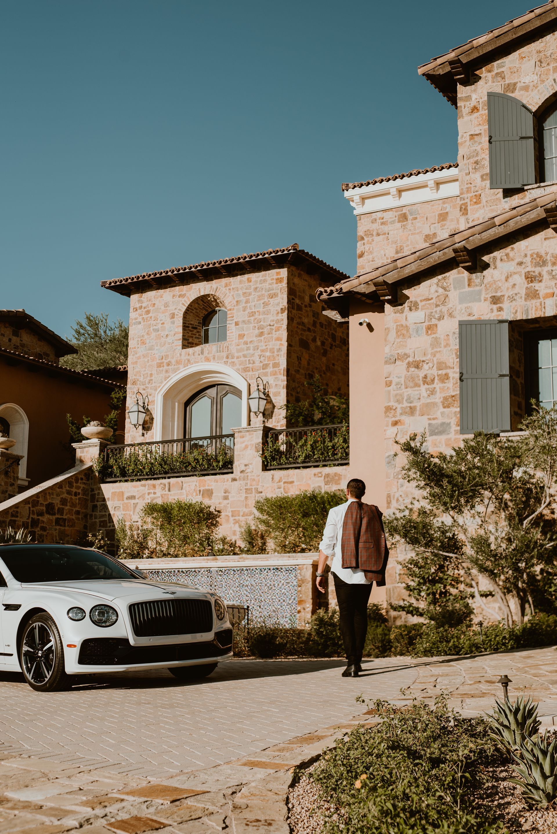 A man is walking towards a white car parked in front of a large stone building.