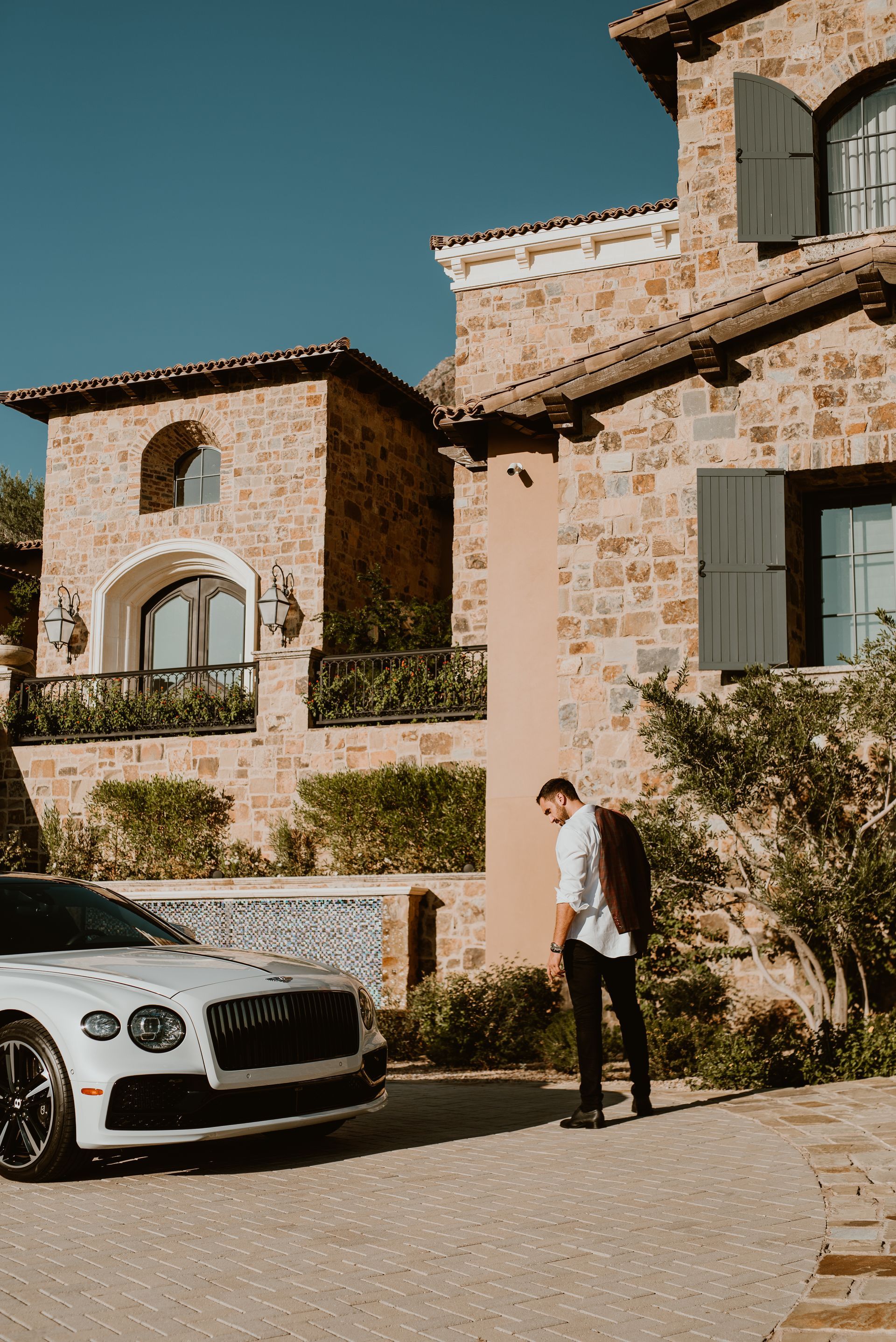 A man is standing in front of a white car parked in front of a stone building.