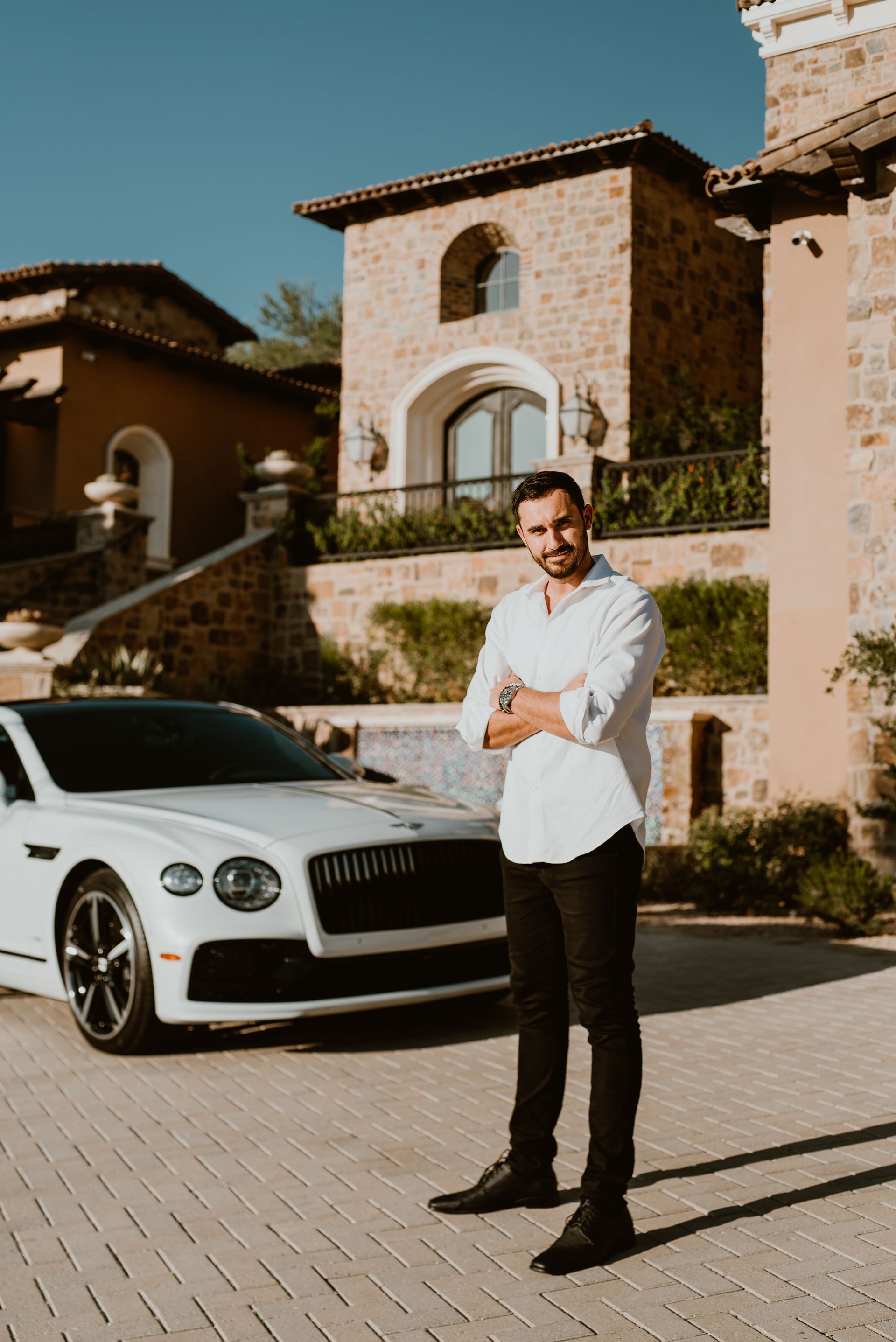 A man is standing in front of a white bentley car.