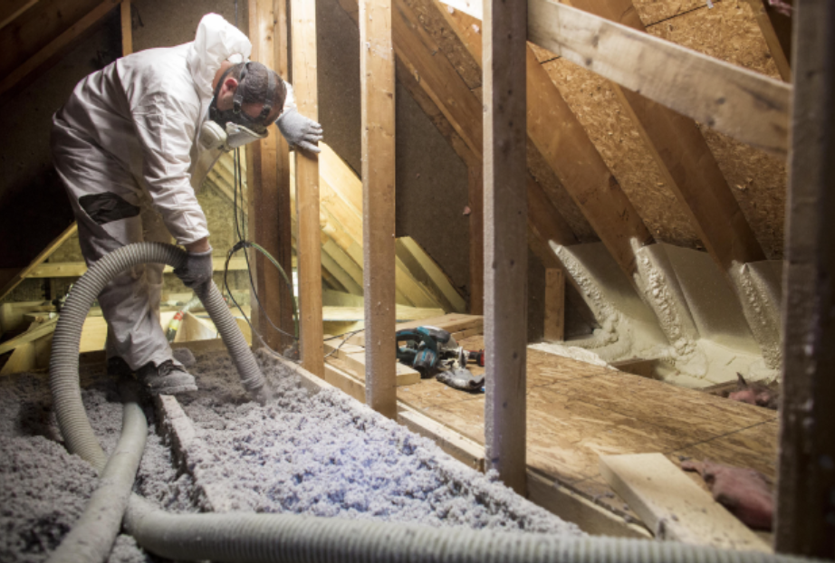 Man in protective suit insulates an attic with white fluffy material.