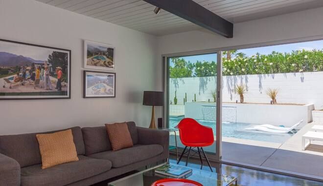 A living room with a couch , chair , coffee table and sliding glass doors leading to a pool.
