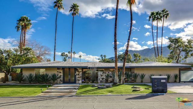 A house with palm trees in front of it and mountains in the background.