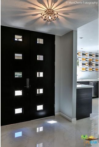 A hallway with a black door and a chandelier hanging from the ceiling.