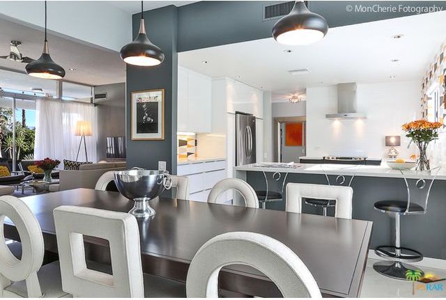 A dining room with a table and chairs and a kitchen in the background
