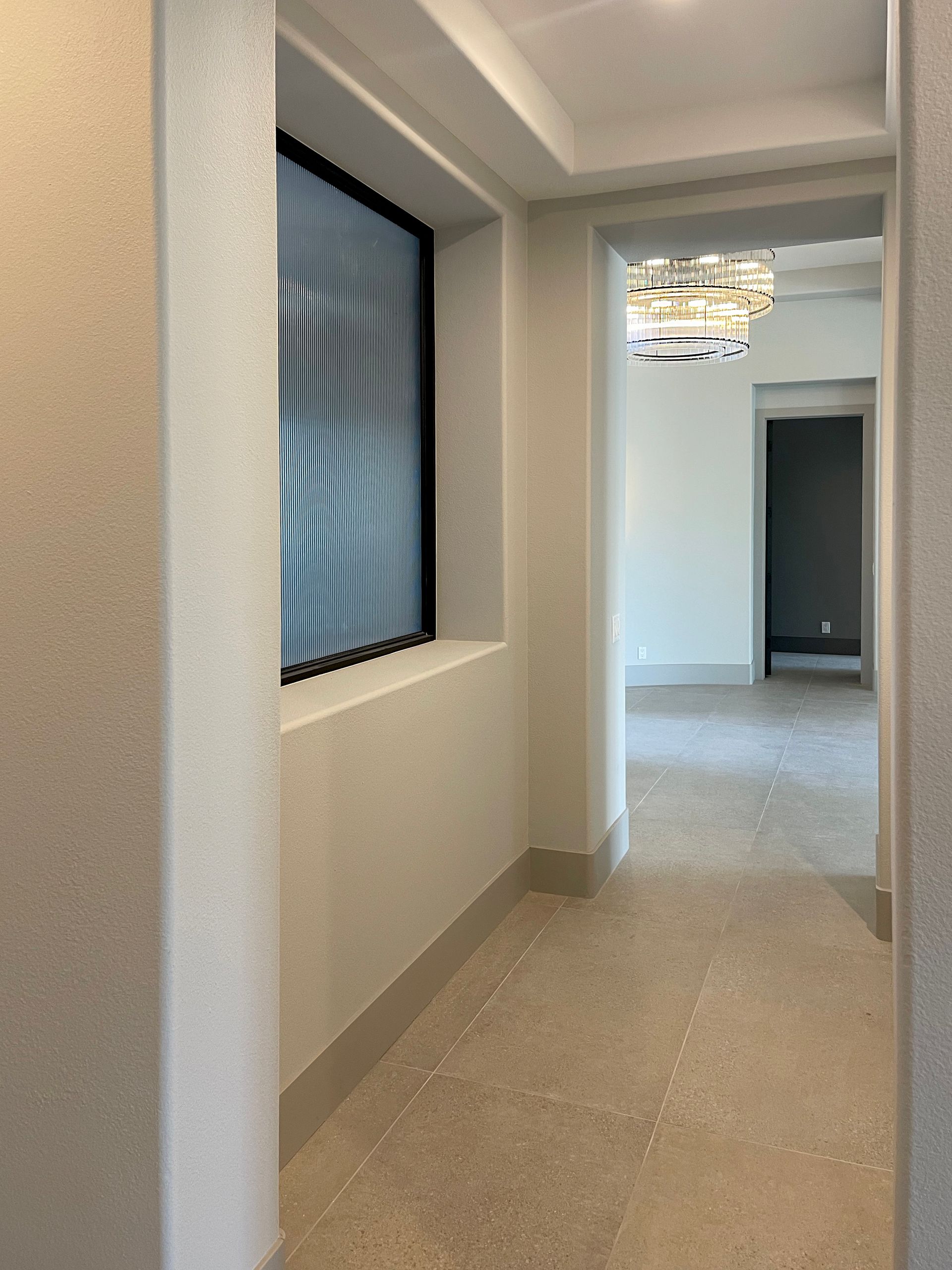 A hallway with a window and a chandelier hanging from the ceiling.