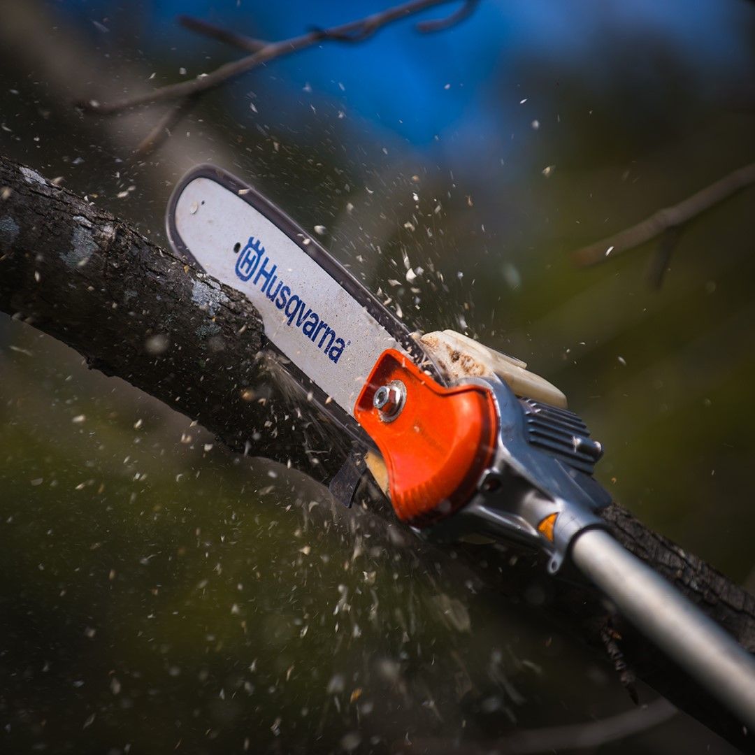 A Husqvarna Chainsaw Is Cutting A Tree Branch — Mid Coast Mowers In Taree, NSW