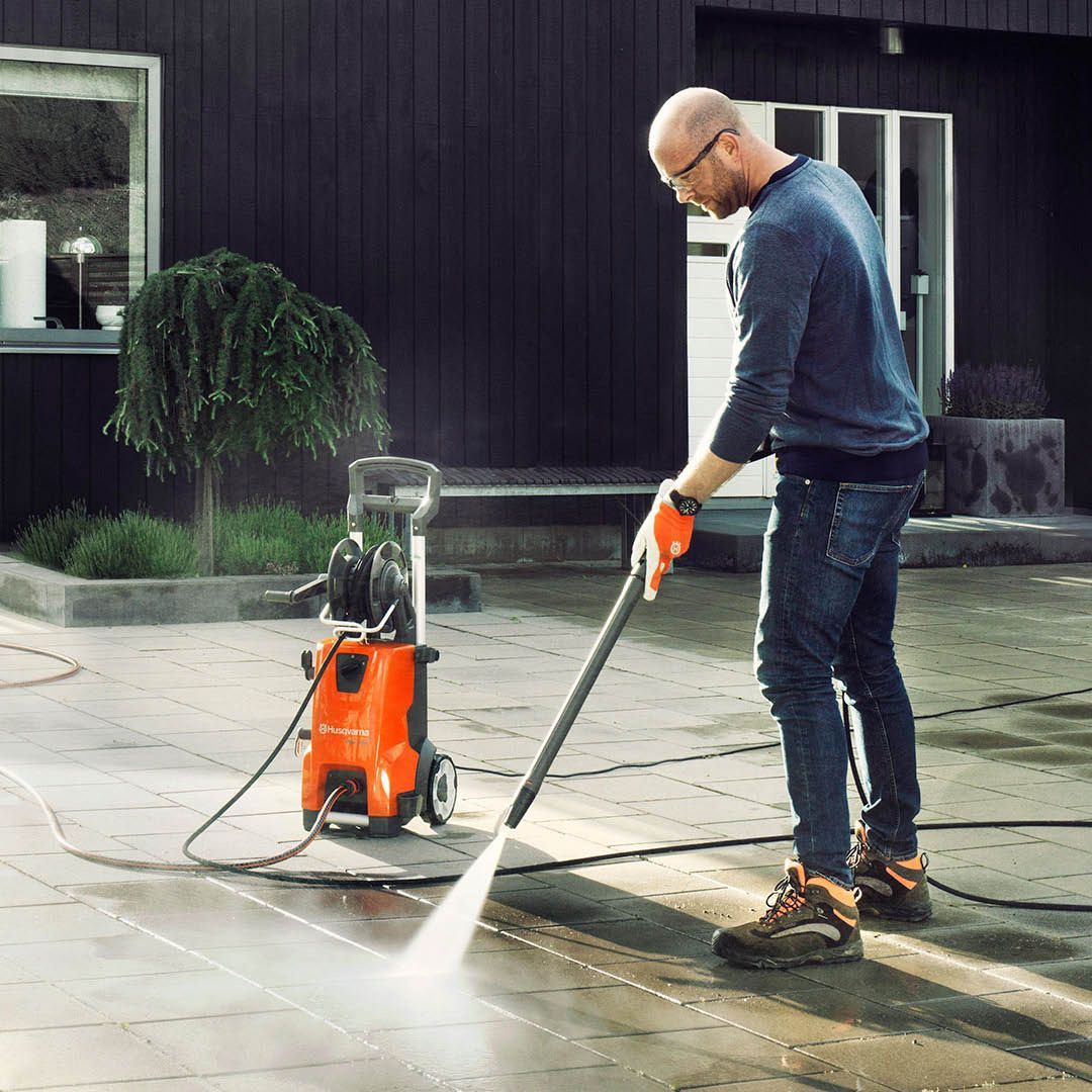 A Man Is Using A High Pressure Washer To Clean A Driveway — Mid Coast Mowers In Taree, NSW