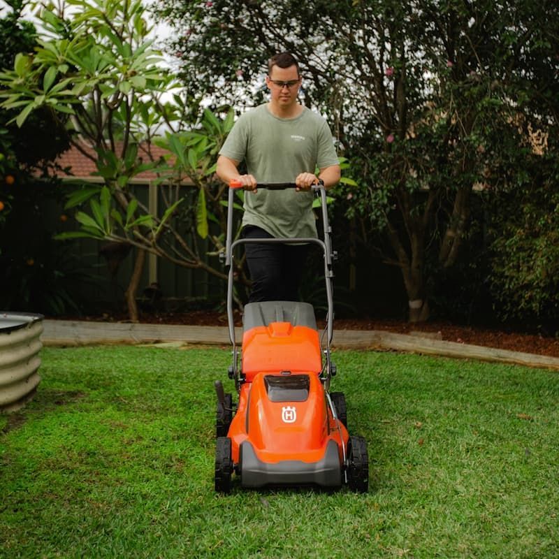 A Man Is Using A Husqvarna Lawn Mower To Cut The Grass — Mid Coast Mowers In Taree, NSW