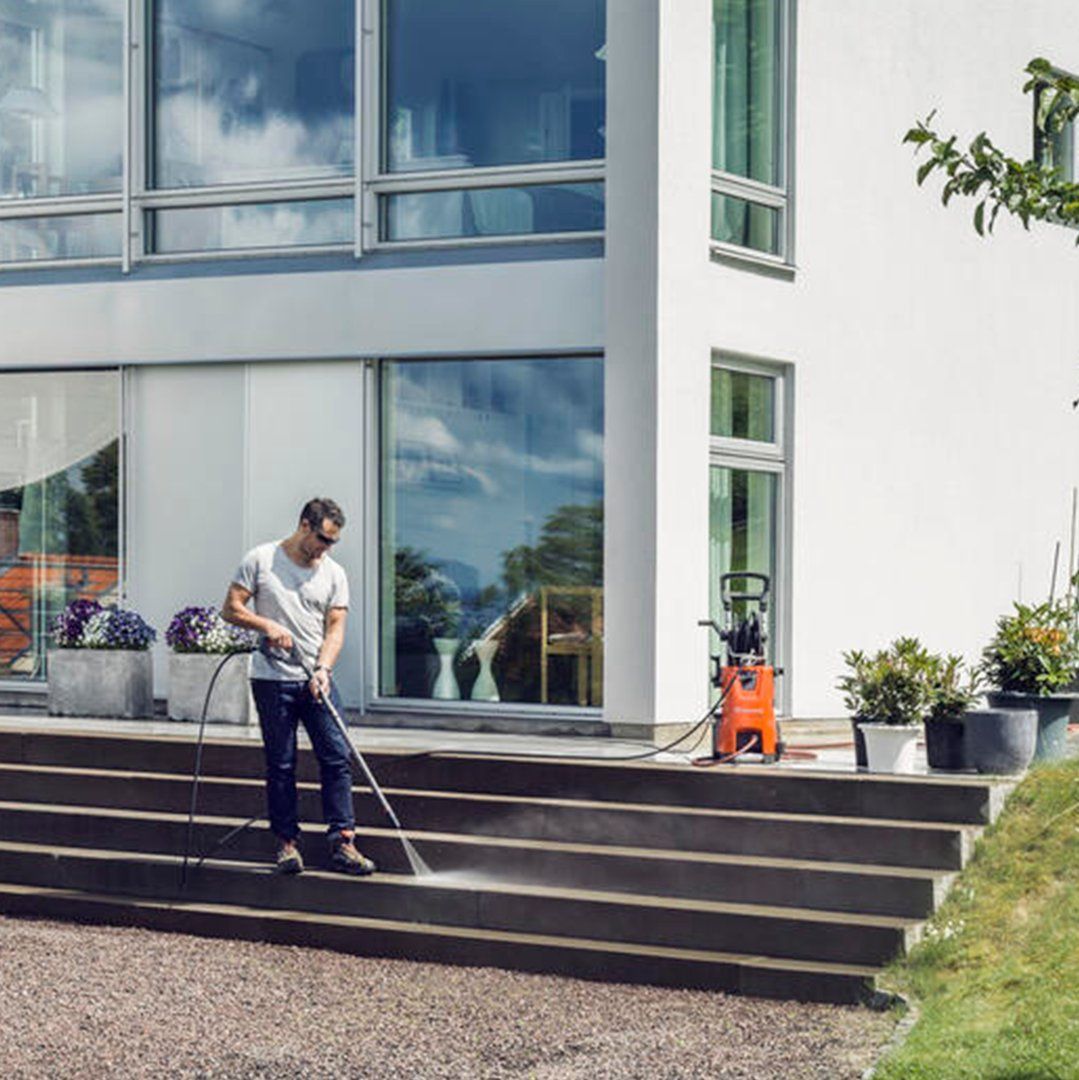 A Man Is Cleaning The Steps Of A House With A High Pressure Washer — Mid Coast Mowers In Taree, NSW
