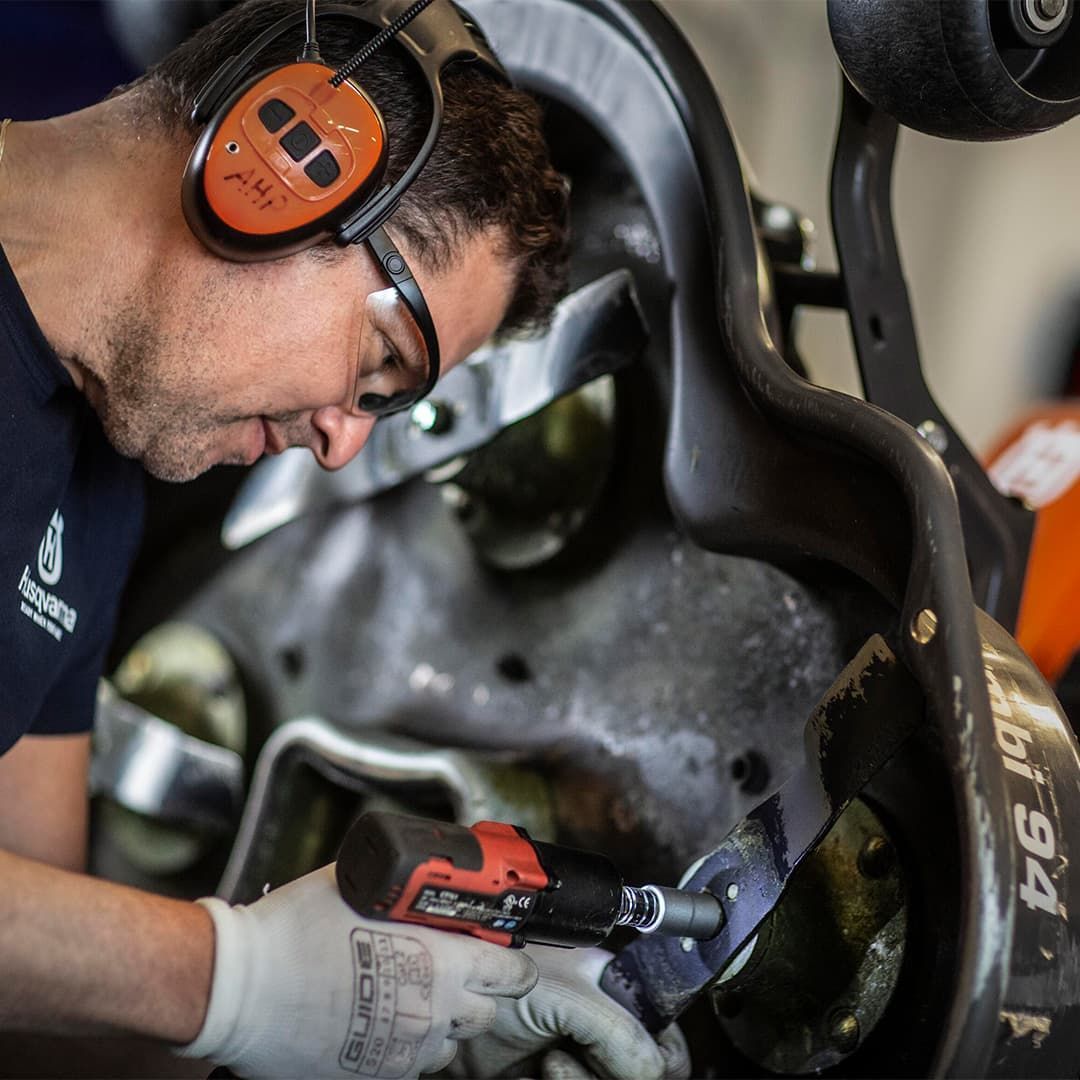 A Man Wearing Headphones And Gloves Is Working On A Machine — Mid Coast Mowers In Taree, NSW
