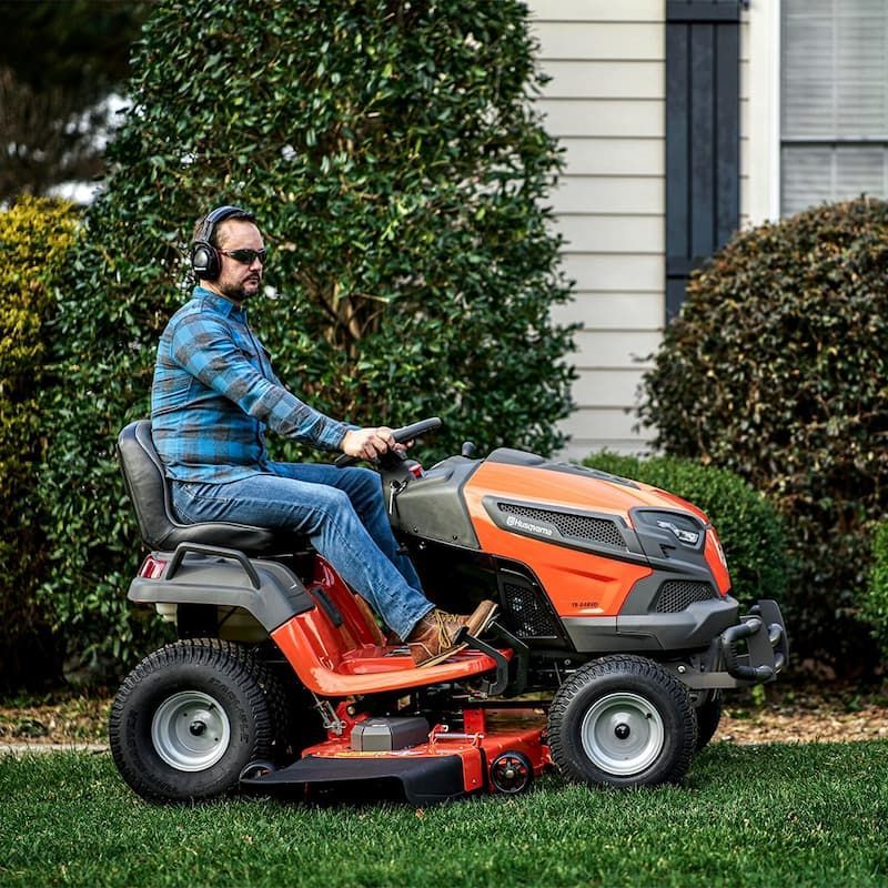 A Man Is Riding A Lawn Mower On A Lush Green Lawn — Mid Coast Mowers In Taree, NSW
