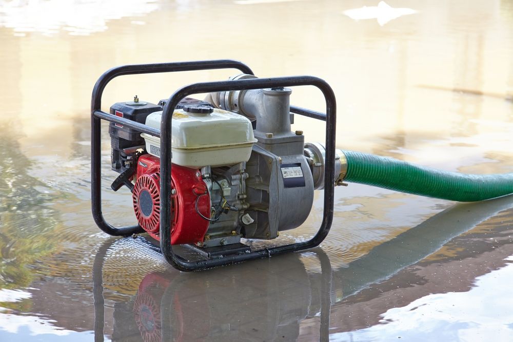 A Water Pump With A Green Hose Attached To It Is Sitting In A Puddle Of Water — Mid Coast Mowers In Taree, NSW