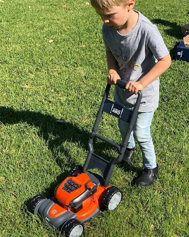 A Young Boy Is Playing With A Toy Lawn Mower On The Grass — Mid Coast Mowers In Taree, NSW