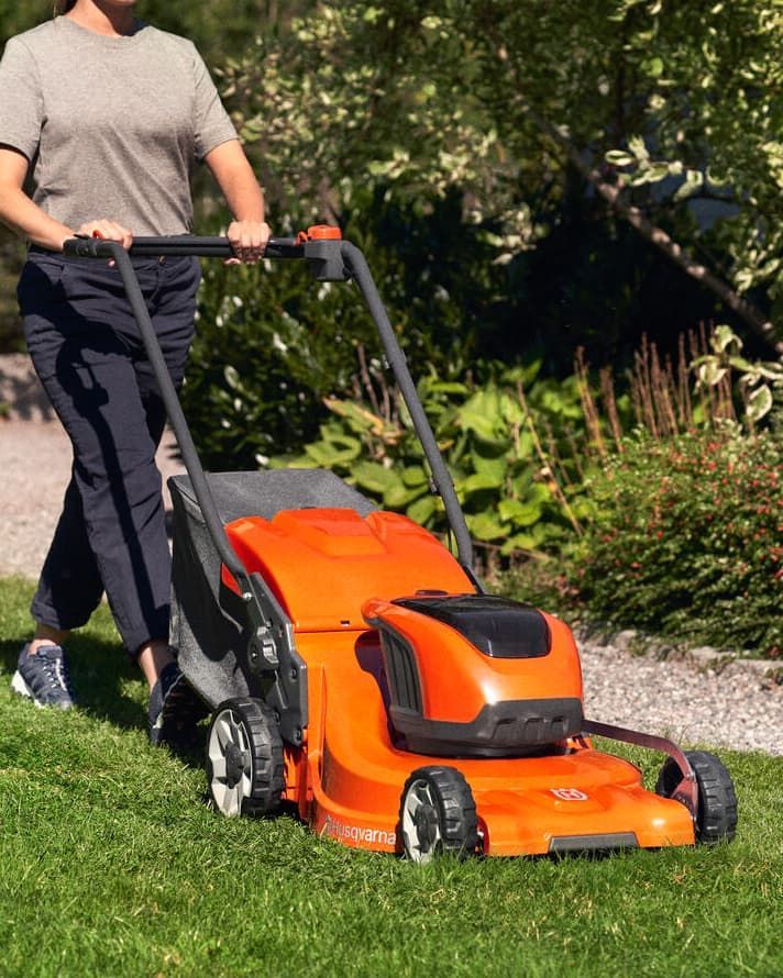 A Woman Is Using An Orange Lawn Mower To Cut The Grass — Mid Coast Mowers In Taree, NSW