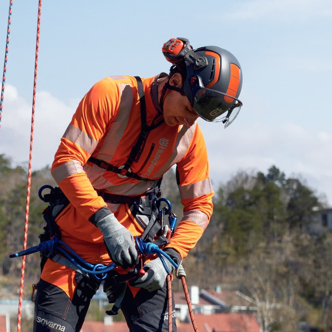 A Man Wearing An Orange Shirt And A Helmet Is Working On A Rope — Mid Coast Mowers In Taree, NSW