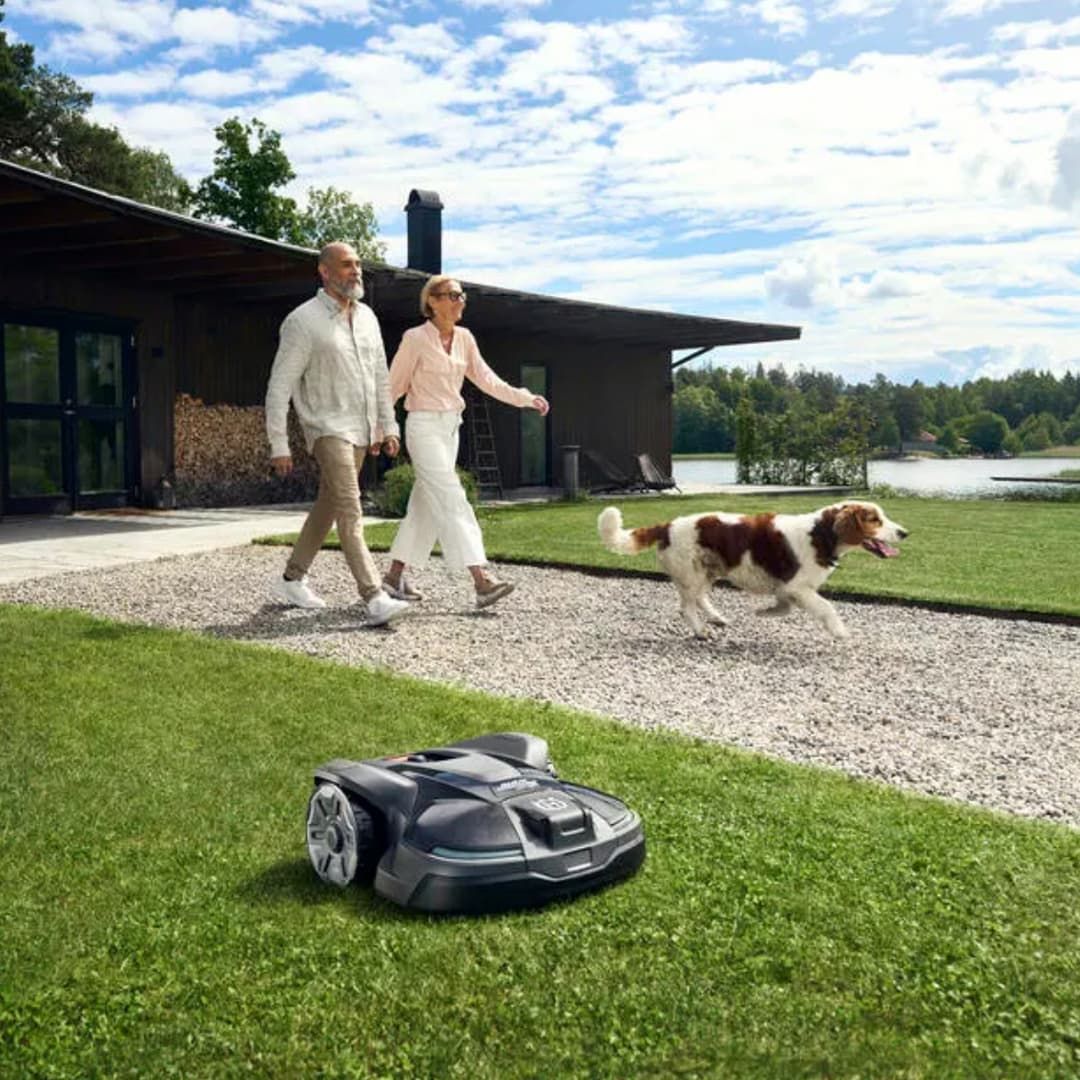 A Man And Woman Are Walking Their Dog Next To A Robotic Lawn Mower — Mid Coast Mowers In Taree, NSW