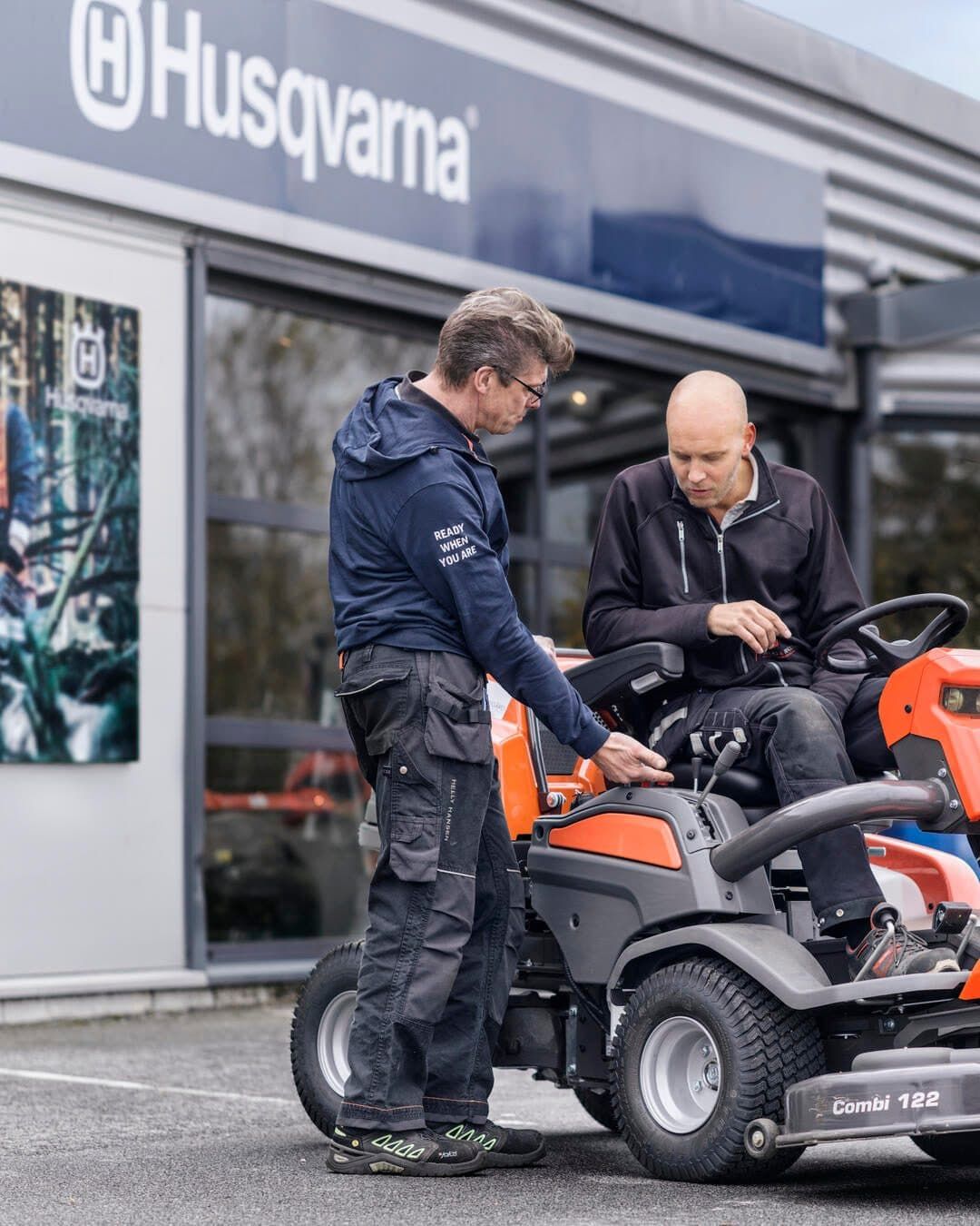 Two Men Are Working On A Lawn Mower In Front Of A Husqvarna Store — Mid Coast Mowers In Taree, NSW