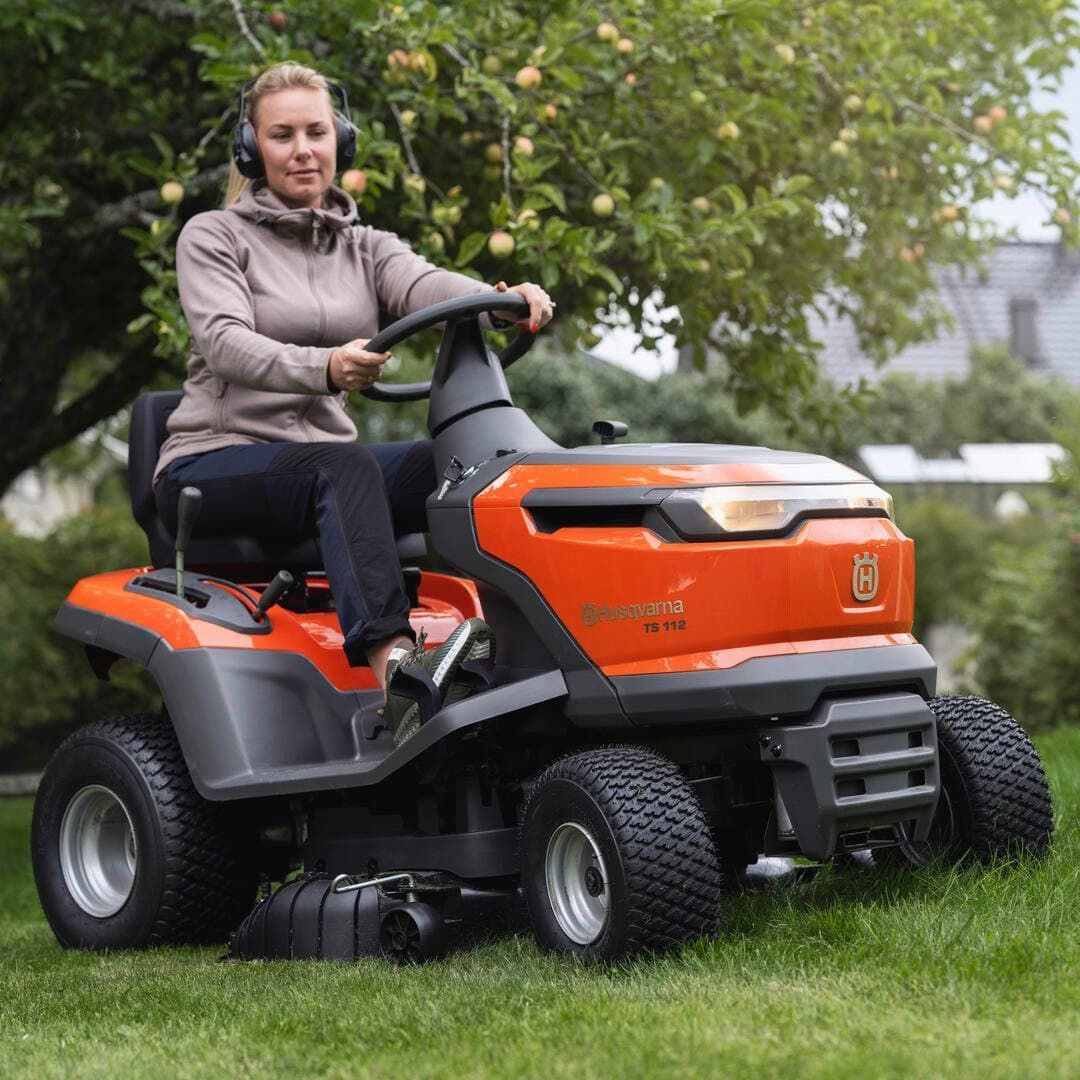 A Woman Is Sitting On A Lawn Mower Wearing Headphones — Mid Coast Mowers In Taree, NSW