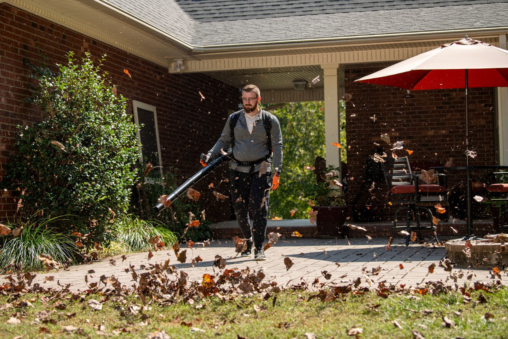 A Man Is Blowing Leaves On The Sidewalk In A Park — Mid Coast Mowers In Taree, NSW