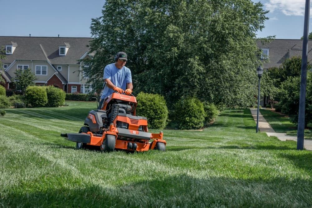Man Mowing a Green Lawn With an Orange Riding Lawnmower — Mid Coast Mowers In Taree, NSW