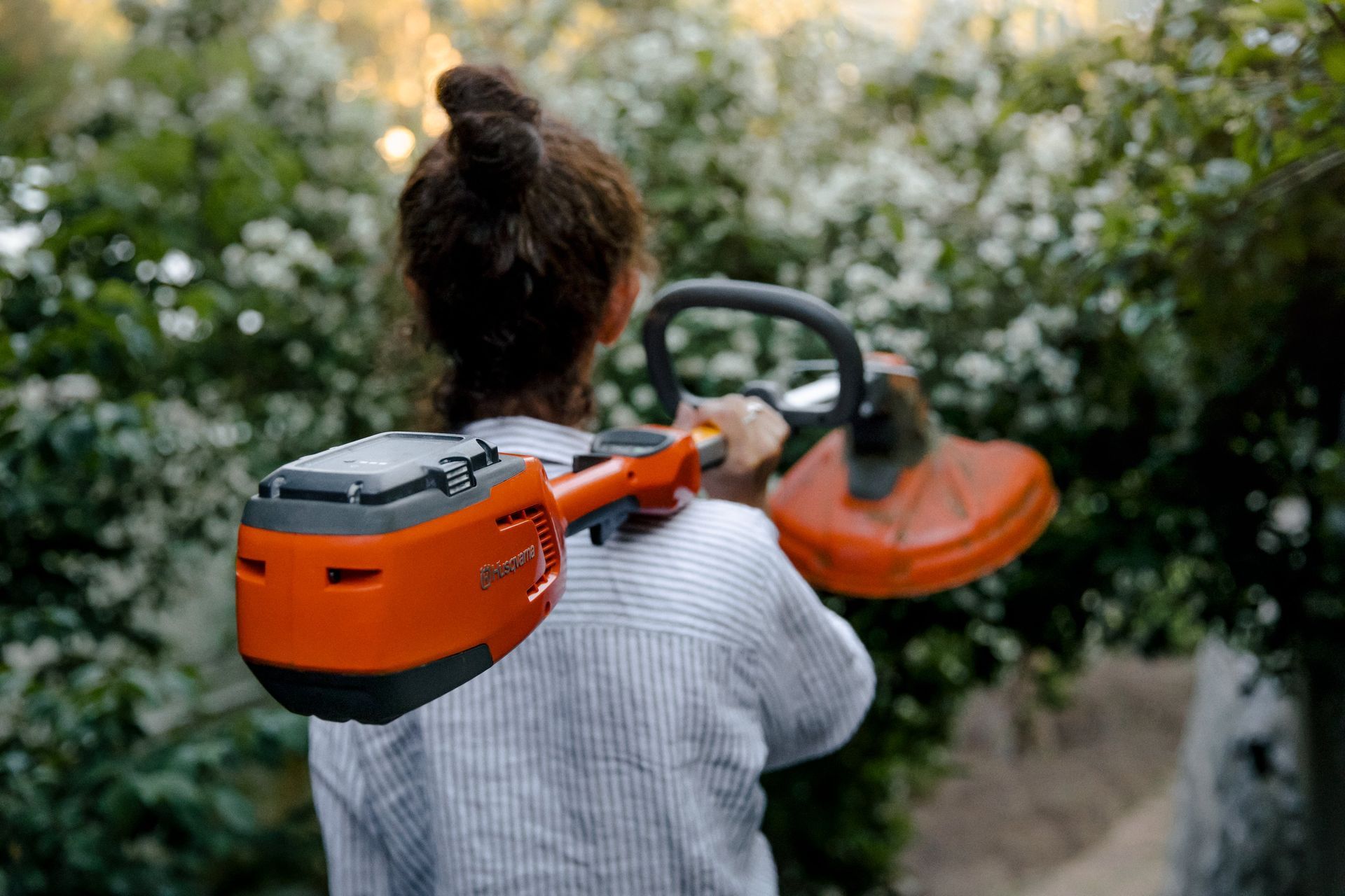 A Woman Is Cutting A Bush With A Hedge Trimmer — Mid Coast Mowers In Taree, NSW