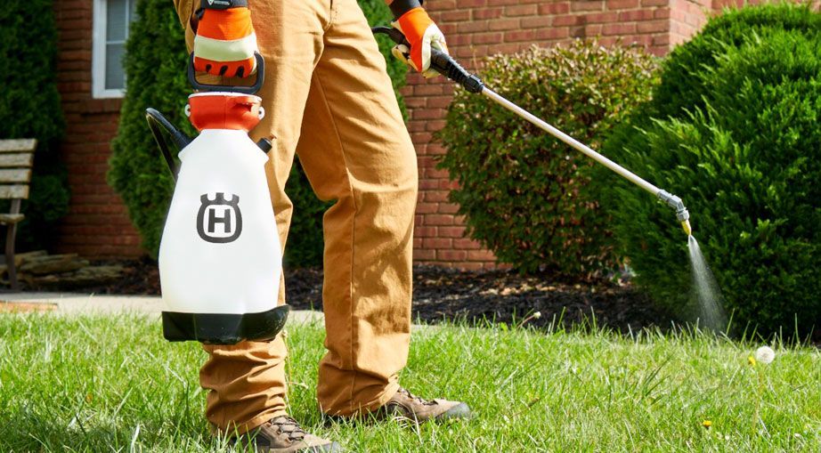 A Man Is Spraying A Lawn With A Husqvarna Sprayer — Mid Coast Mowers In Taree, NSW