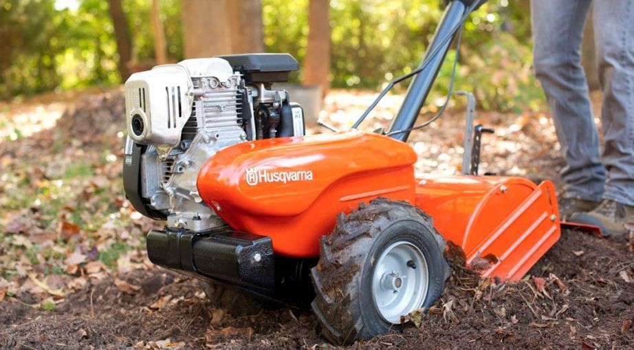 A Person Is Using A Small Orange Tractor To Dig A Hole In The Ground — Mid Coast Mowers In Taree, NSW