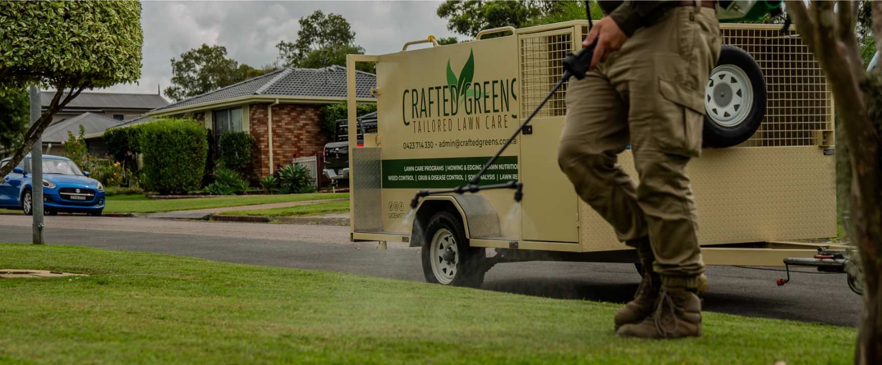 A Person Spraying a Lawn With a Trailer in a Residential Area — Mow & Mulch Lawn & Garden Maintenance In Corlette, NSW