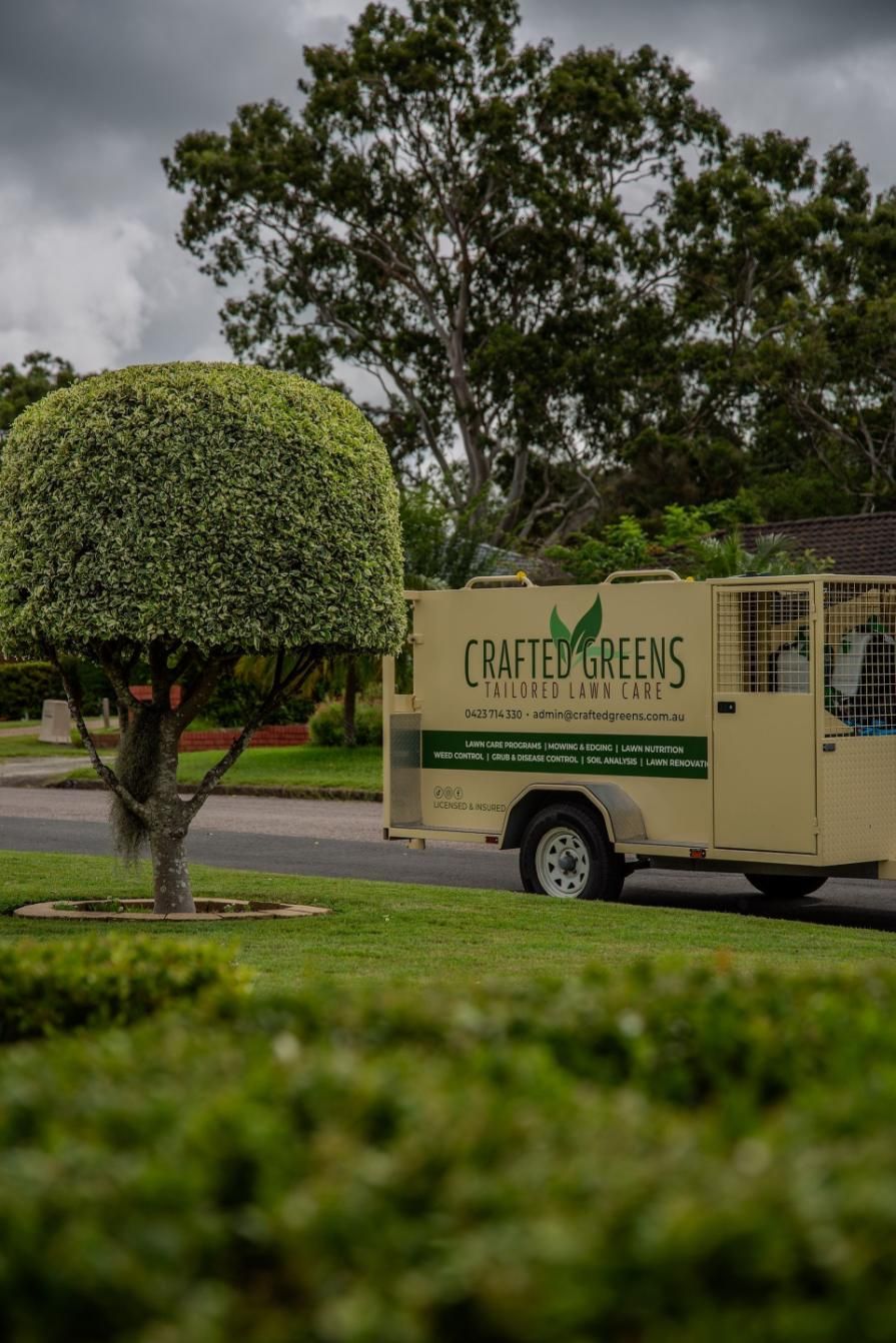 A Person Spraying Grass With a Pesticide Near a Trailer in a Suburban Neighborhood — Mow & Mulch Lawn & Garden Maintenance In Soldiers Point, NSW