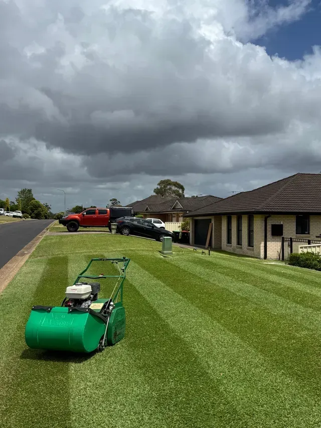Lawn mower on striped green lawn beside brick houses under dark storm clouds — Mow & Mulch Lawn & Garden Maintenance In Nelson Bay, NSW