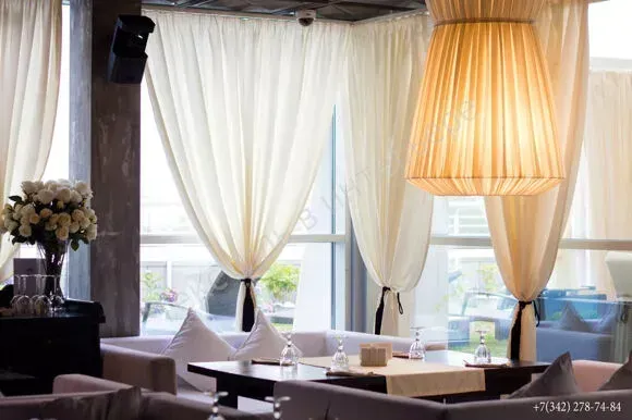Elegant restaurant lounge with sheer white curtains, beige lampshade, and tables by bright windows
