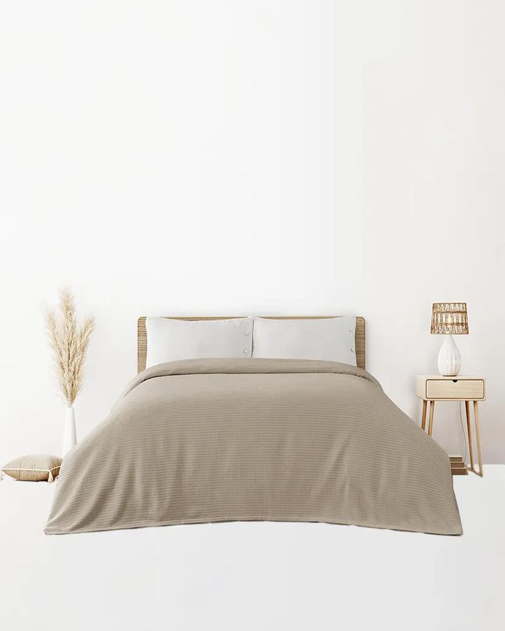 Minimalist beige bed with white pillows, small side table, lamp, and vase in a bright room
