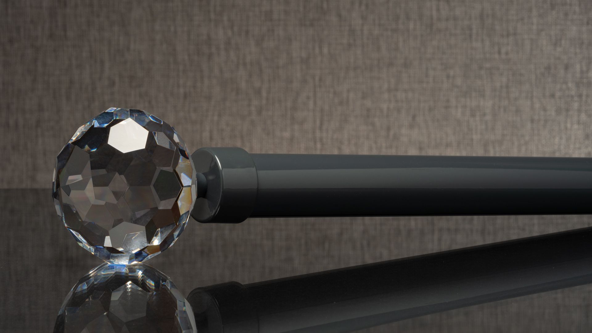 Faceted crystal ball on a black rod, reflecting on a dark surface against a gray background