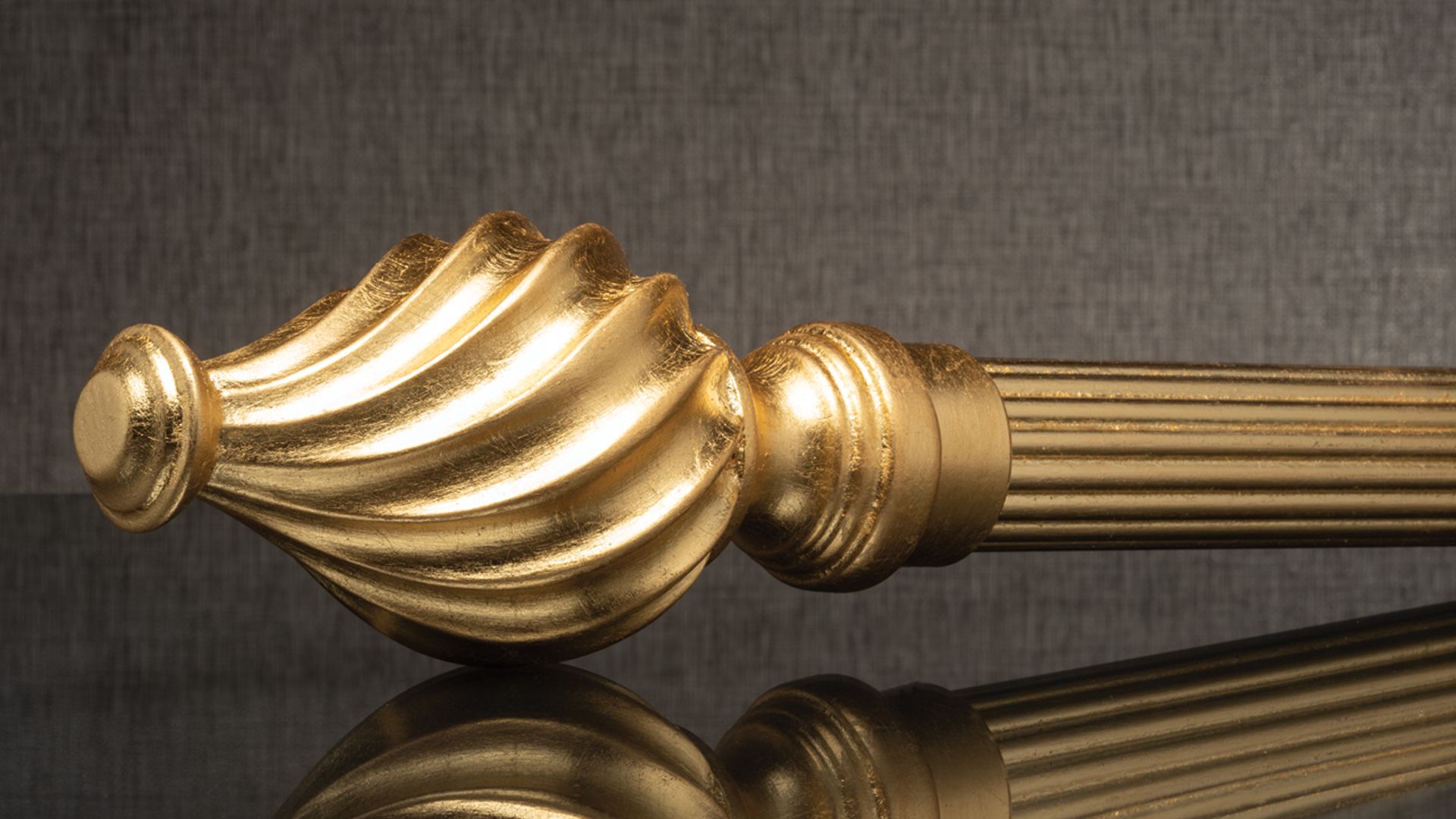 Gold ornamental curtain rod finial with ribbed shaft on a dark textured background