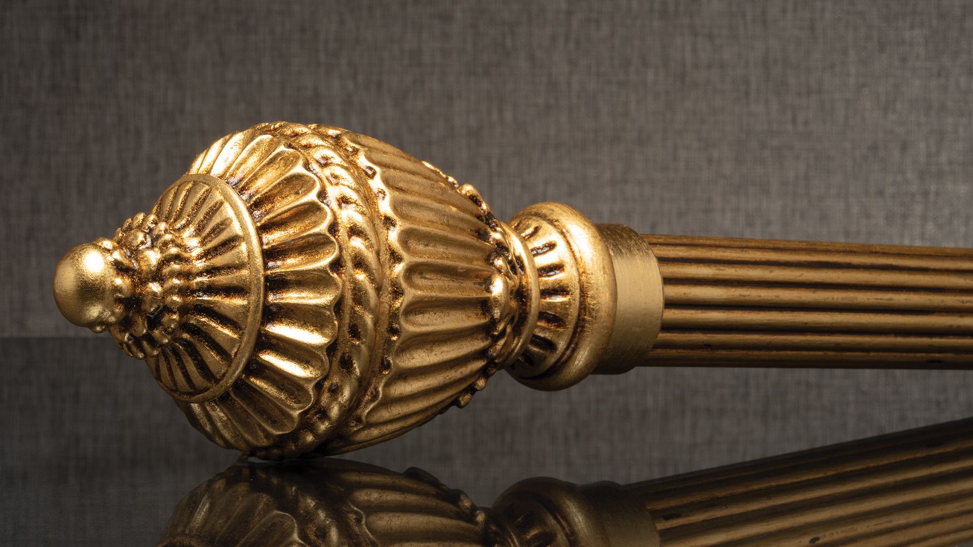 Gold ornamental curtain rod finial with ribbed shaft on a dark background