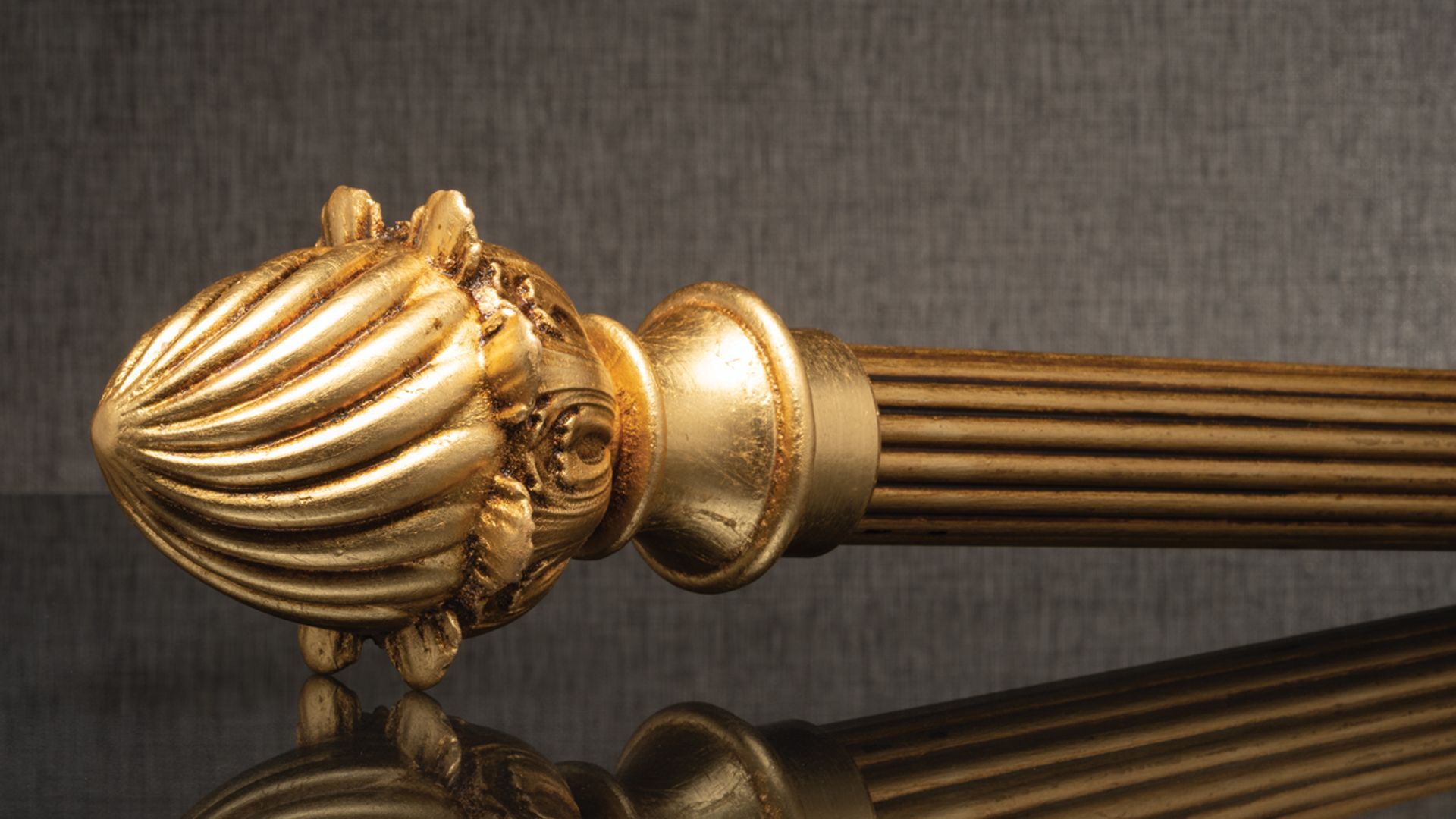Gold decorative curtain rod finial with ribbed, shell-like design on a dark surface