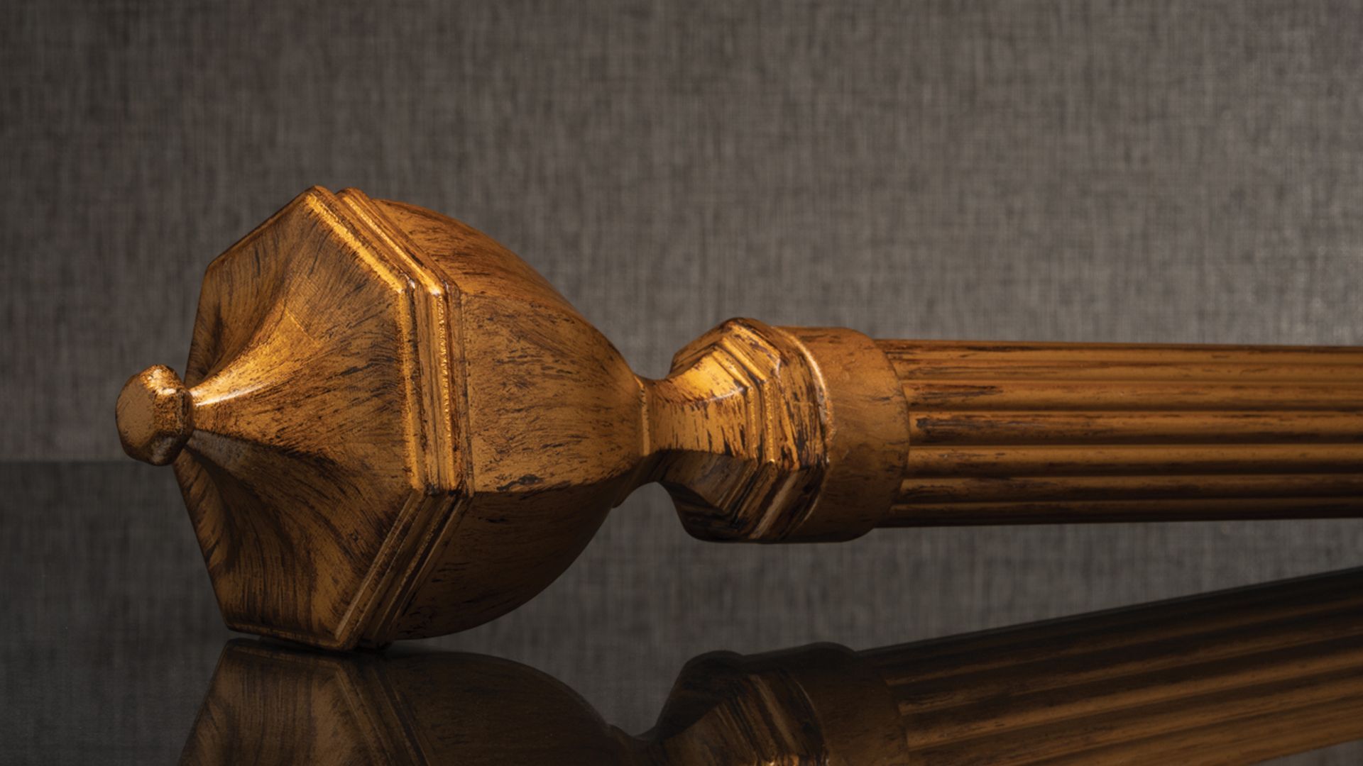 Wooden ornamental staff or scepter with a carved golden-brown head on a dark reflective surface
