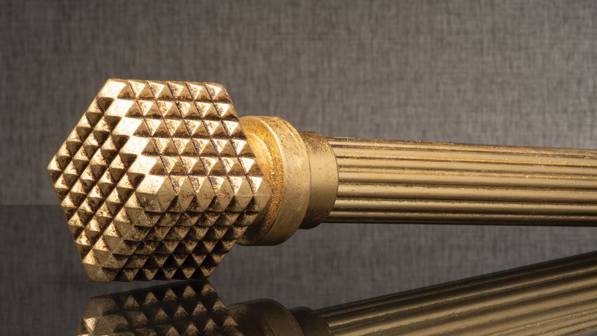 Close-up of a gold, textured massage tool with a ribbed handle on a dark reflective surface