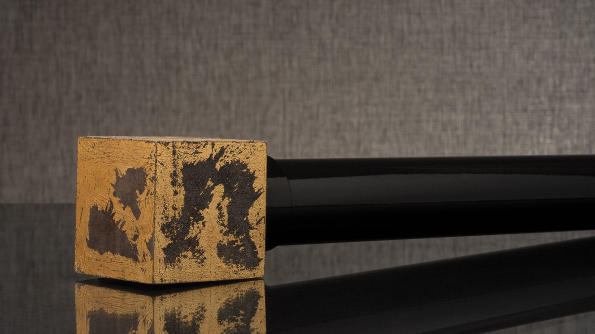 Gold and black textured rectangular object with a long black handle on a dark reflective surface