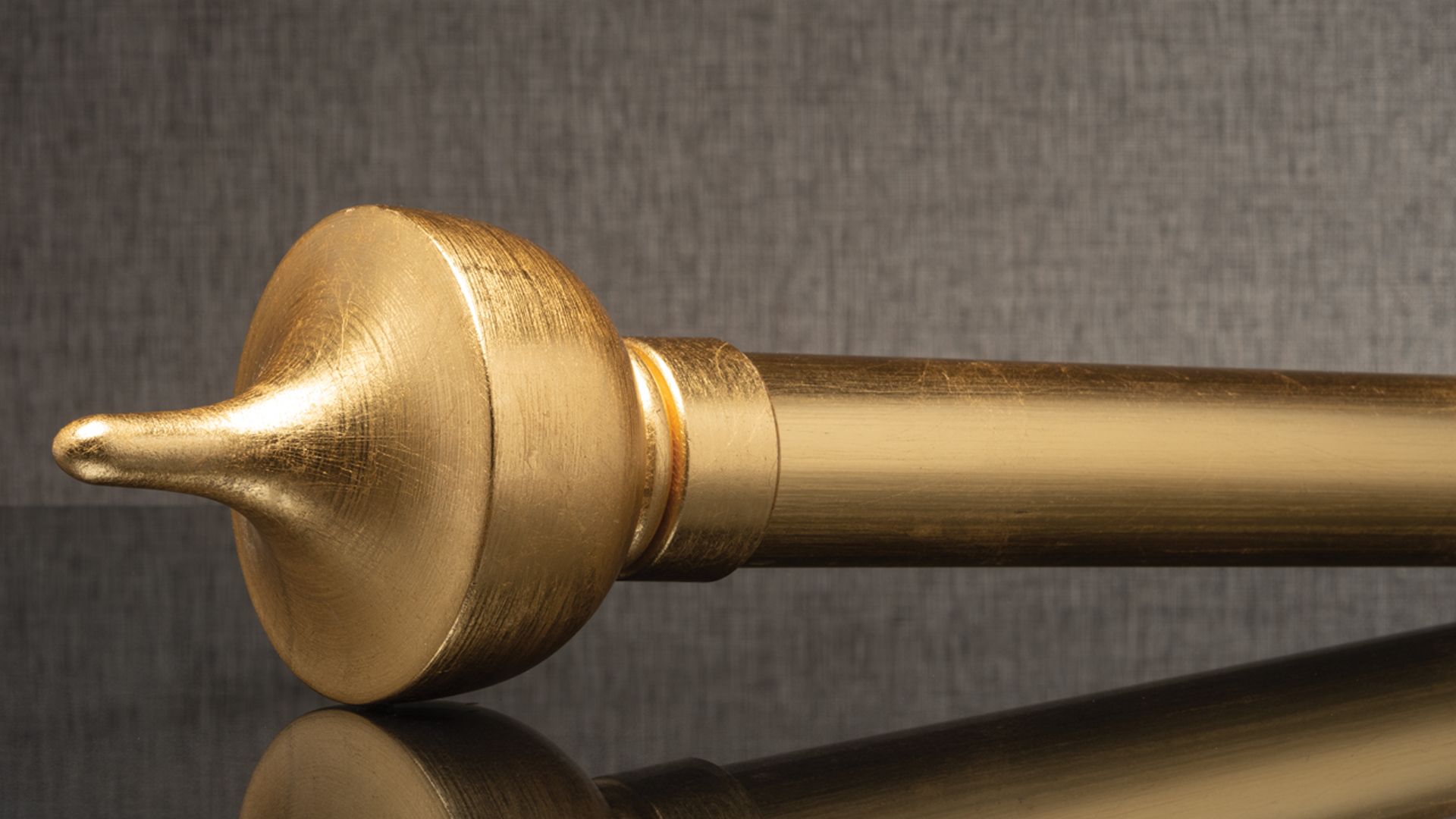 Gold curtain rod finial on a dark reflective surface, close-up side view