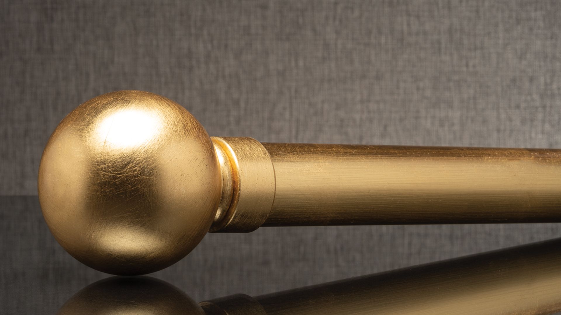 Golden metal bar with a spherical end on a dark reflective surface