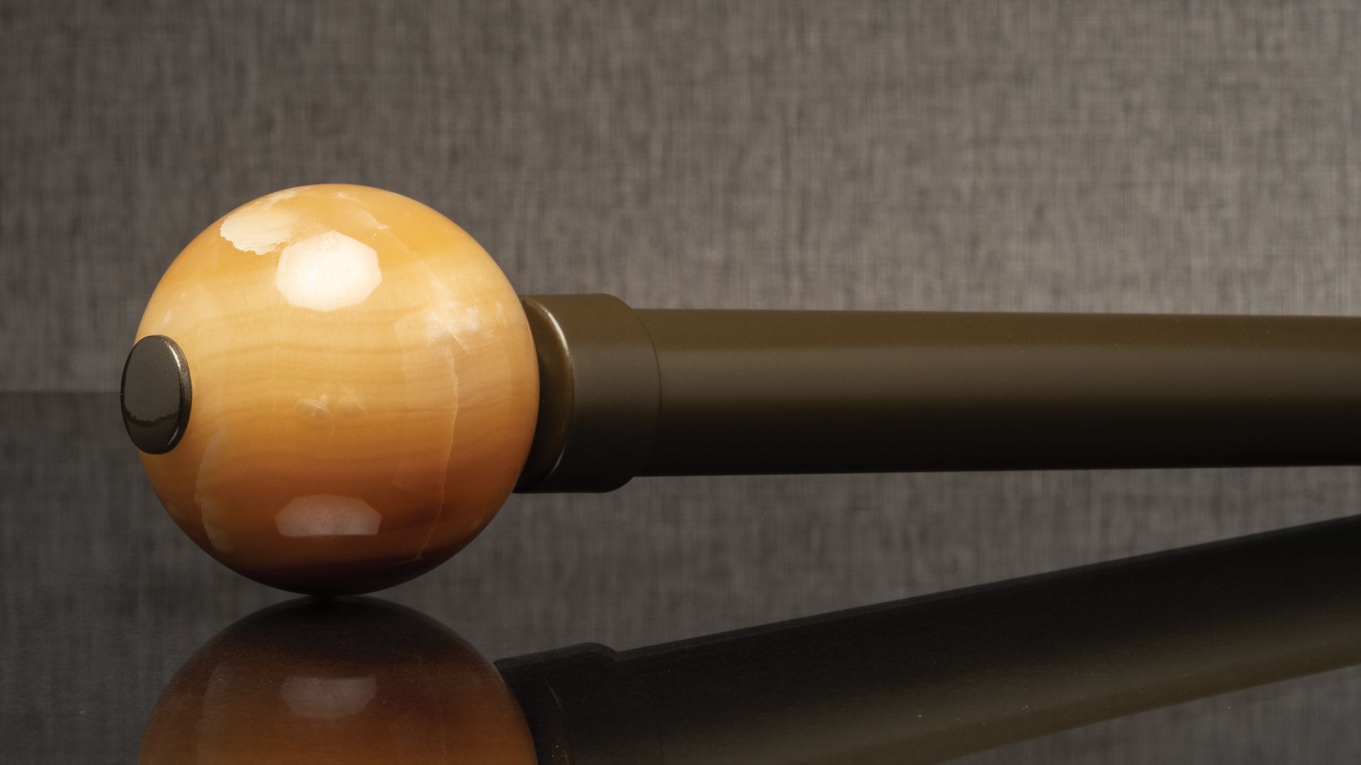 Close-up of a wooden massage hammer with a round amber head and black handle on a gray surface