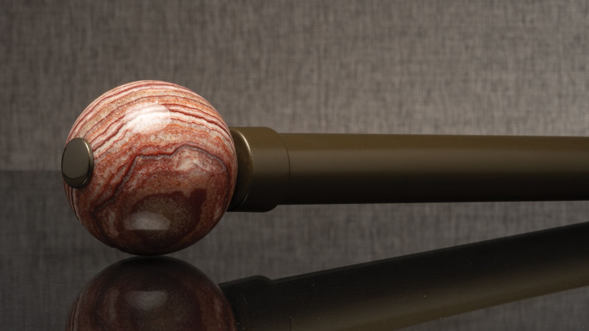 Close-up of a marbled red-and-white billiard cue ball attached to a dark wooden cue on a reflective surface