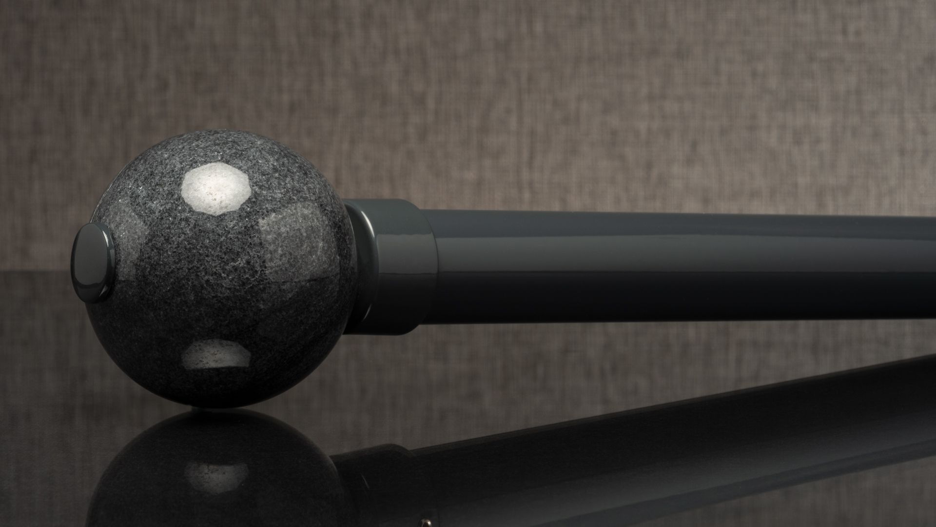 Black speckled massage roller with a long handle on a reflective surface