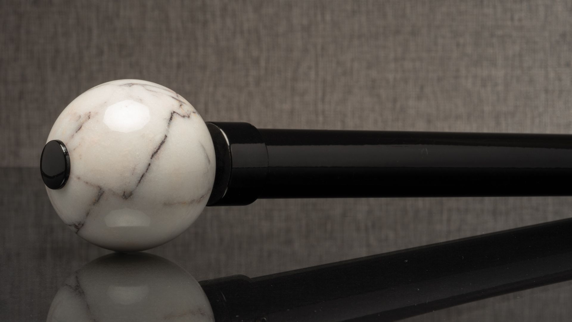 White marble-like ball mounted on a black rod against a gray background
