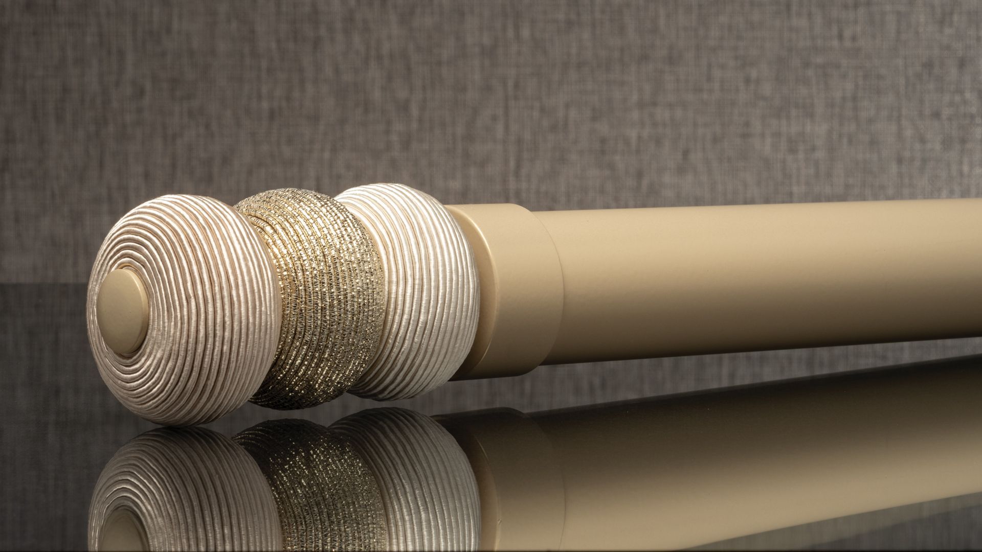 Three textured silver and gold spheres on beige rods against a reflective dark background
