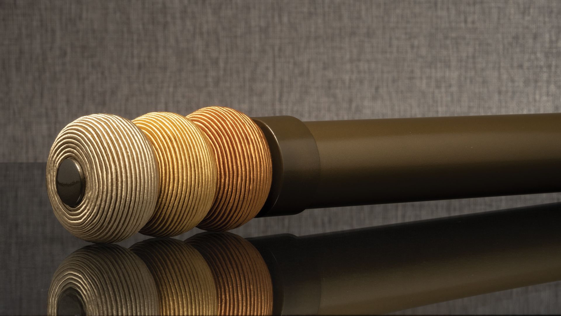 Three textured metallic spheres beside a dark cylindrical rod on a reflective surface.