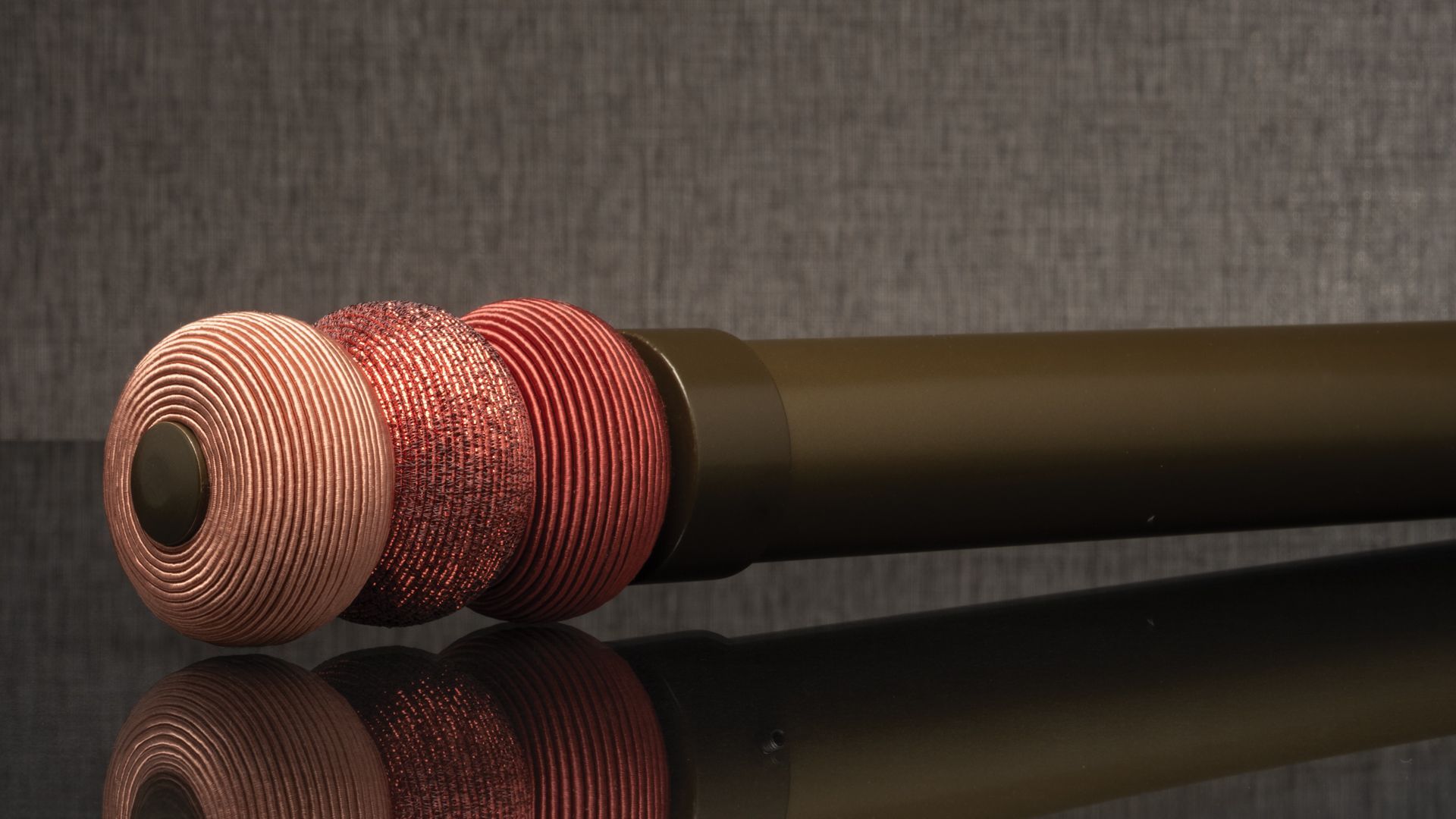 Three red-and-white textured metal caps on a black cylindrical rod, reflected on a glossy surface