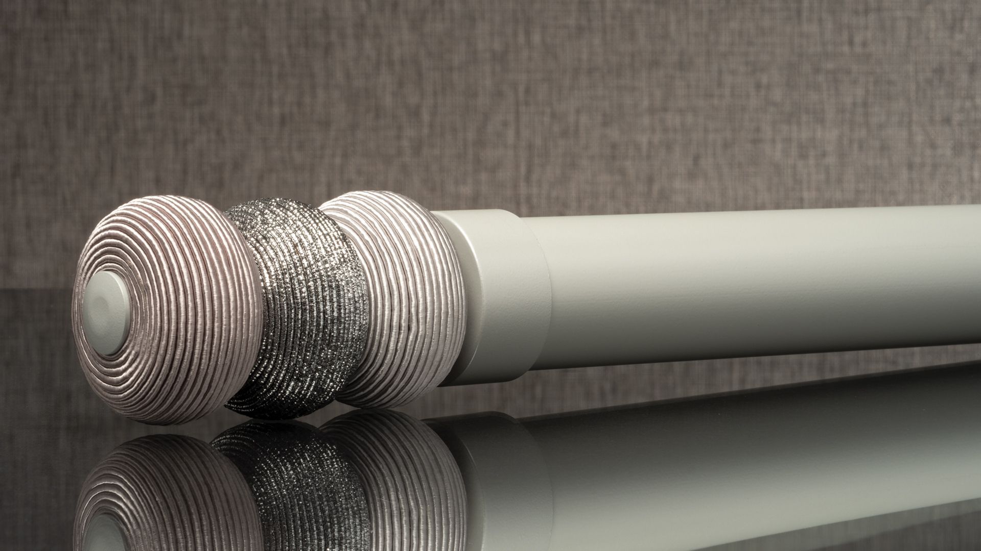 Three patterned silver exercise hand grippers beside a light gray cylindrical handle on a reflective surface